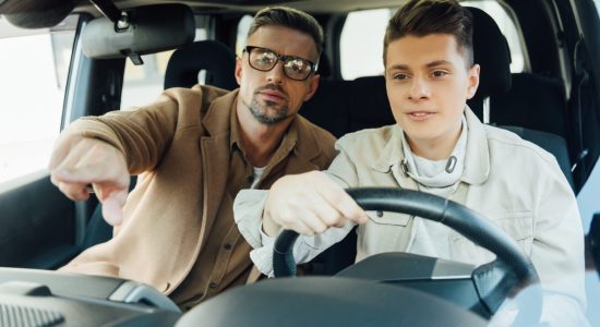 handsome father pointing on something while teaching teen son driving car